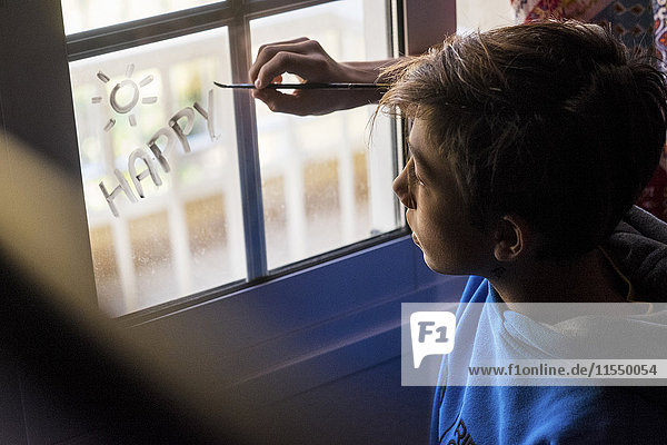 Junge malt das Wort'Glücklich' auf Fensterscheibe
