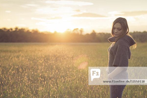 Woman wearing turtleneck pullover standing on a meadow at backlight