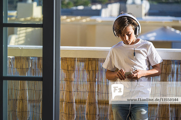 Junge hört Musik mit Kopfhörer und Smartphone auf dem Balkon