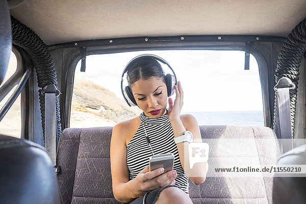 Spanien  Teneriffa  junge Frau sitzt auf dem Rücksitz eines Autos und hört Musik mit Kopfhörern.