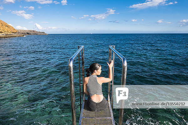 Spanien  Teneriffa  junge Frau auf einer Plattform vor dem Meer sitzend