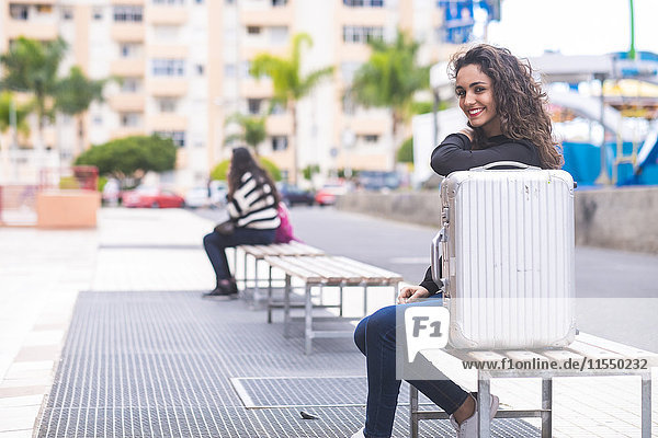 Spanien  Teneriffa  Porträt eines lächelnden Teenagermädchens auf einer Bank sitzend mit ihrem Koffer