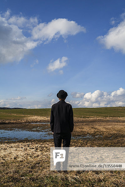 Back view of young man dressed in black standing on pasture