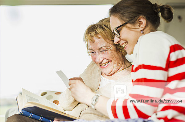 Happy senior woman and young woman sitting on couch looking at photo album