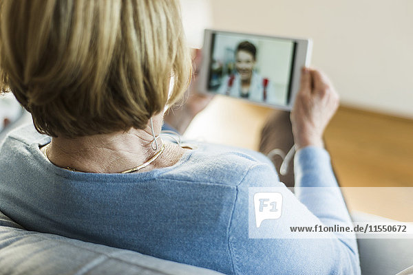 Seniorin betrachtet Bild eines jungen Mannes auf digitalem Tablett