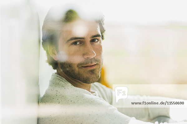 Porträt eines entspannten jungen Mannes mit Blick durch die Fensterscheibe