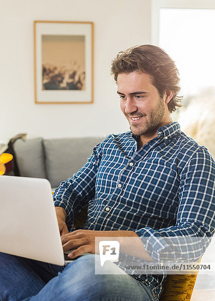 Portrait of smiling young man sitting in the living room using laptop