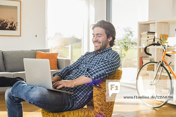 Portrait of smiling young man sitting on armchair in the living room using laptop