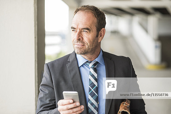 Businessman holding cell phone looking around