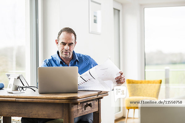 Businessman at home with laptop and plan at wooden table