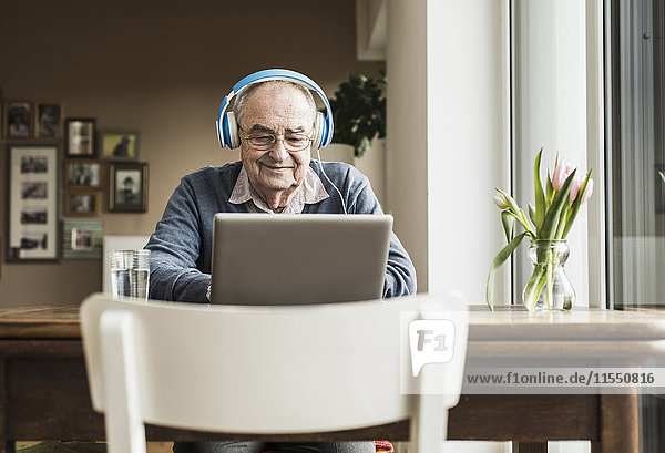 Senior Mann mit Laptop und Kopfhörer zu Hause