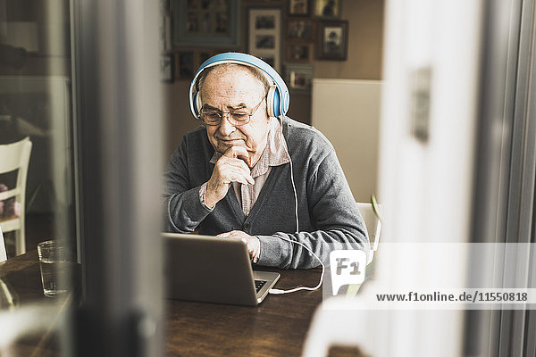 Senior man using laptop and headphones at home