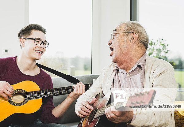Älterer Mann singt und spielt Gitarre mit seinem Enkel.