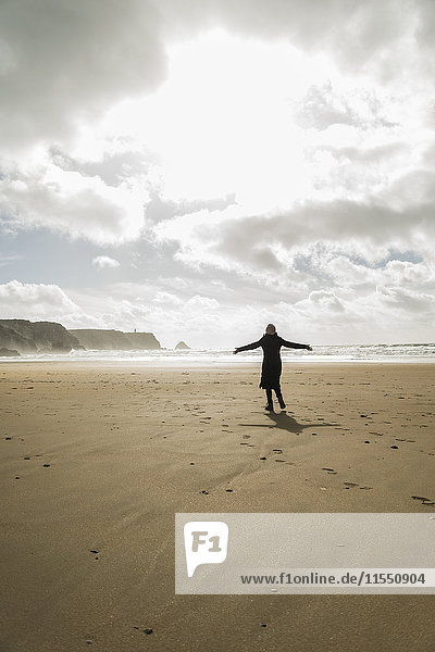 France  Bretagne  Finistere  Crozon peninsula  woman standing on the beach with outstretched arms