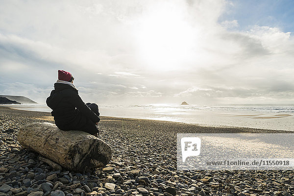 Frankreich  Bretagne  Finistere  Halbinsel Crozon  Frau sitzt auf einem Baumstamm am Strand