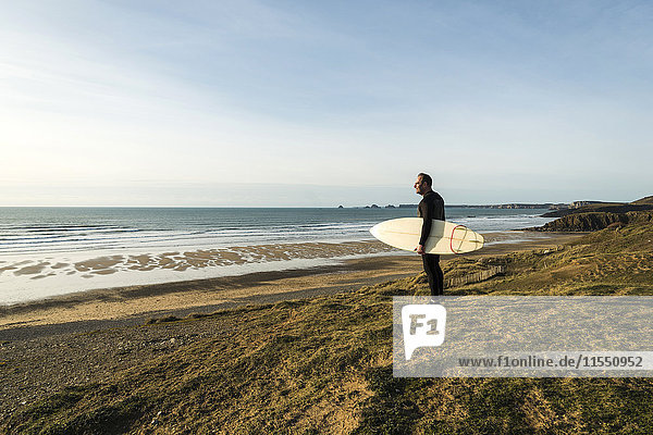 Frankreich  Bretagne  Finistere  Halbinsel Crozon  Mann an der Küste stehend mit Surfbrett