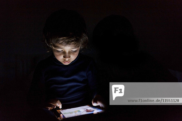 Kleiner Junge im Dunkeln spielt mit digitalem Tablett