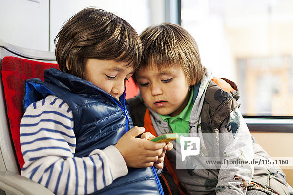 Zwei kleine Jungs sitzen in einem Bus und spielen mit dem Smartphone.