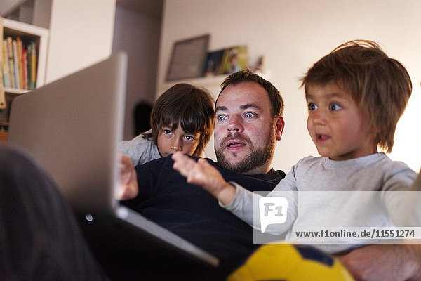 Vater und seine zwei kleinen Söhne schauen sich das Video auf dem Laptop zu Hause an.