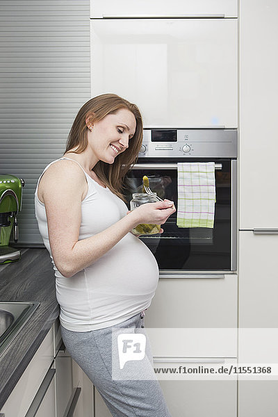 Pregnant woman in kitchen eating gherkins