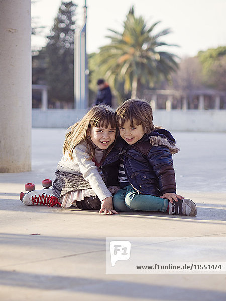 Spain  Girona  smiling little boy and girl sitting side by side on the ground
