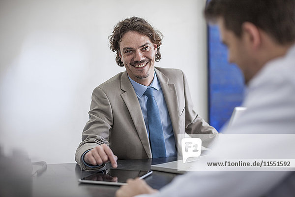Smiling businessman at desk with laptop looking at man
