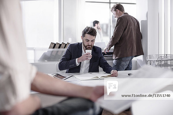 Man sitting at desk drinking coffee in busy office