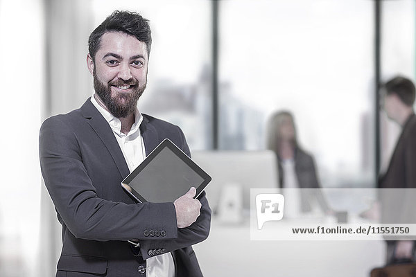 Portrait of smiling businessman holding digital tablet in office