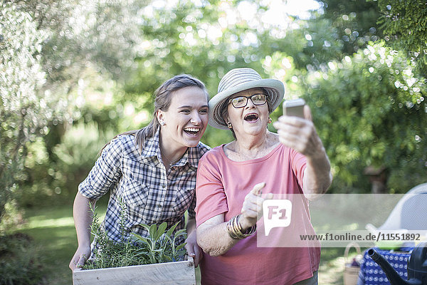Fröhliche Seniorin und Teenagerin bei der gemeinsamen Gartenarbeit mit einem Selfie
