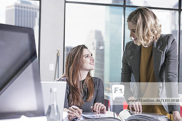 Two smiling women in office looking at each other