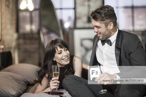 Smiling couple in elegant clothing drinking champagne in bed