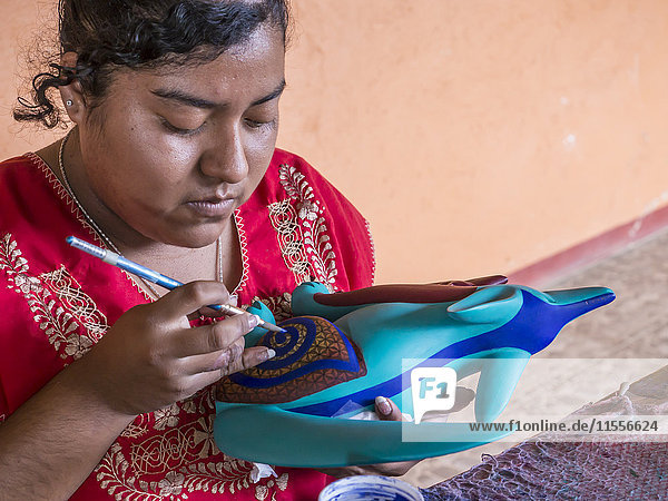 Woman painting a colorful carved wooden figure (alebrije) of a wolf Oaxaca area Mexico North America