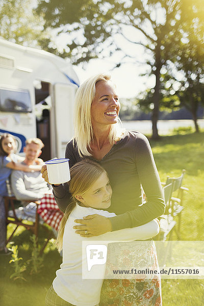 Smiling mother and daughter hugging outside sunny motor home
