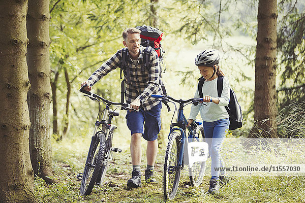 Vater und Tochter mit Rucksäcken Wandern Mountainbikes im Wald
