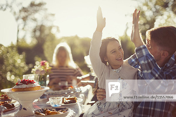 Playful father and daughter high-fiving at sunny garden party patio table