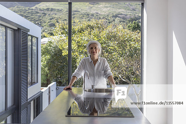 Portrait confident mature woman standing in modern home showcase interior kitchen