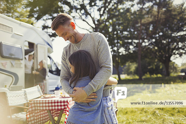 Smiling father hugging daughter outside sunny motor home