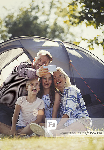 Glückliche Familie nimmt Selfie mit Fotohandy außerhalb des sonnigen Zeltplatzes.