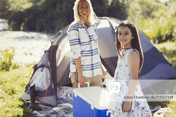 Portrait lächelnde Mutter und Tochter mit Kühlbox vor dem sonnigen Campingplatzzelt