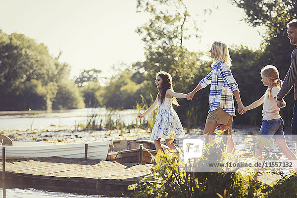 Familie beim Händchenhalten und Spazierengehen am sonnigen Ufer des Sees