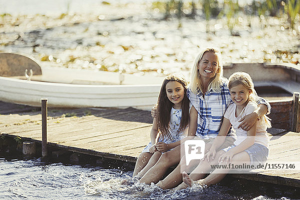 Portrait happy mother and daughters on dock splashing feet in lake