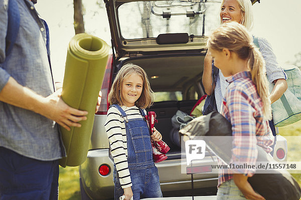 Portrait lächelndes Mädchen mit Familie beim Entladen der Campingausrüstung aus dem Auto