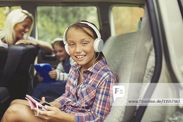 Portrait smiling girl with headphones using digital tablet in back seat of car