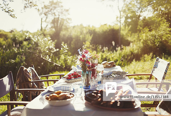 Essen und Blumenstrauß auf sonnigem Gartenparty-Tisch