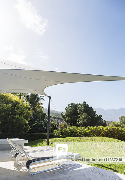 Sonnige  moderne  luxuriöse Terrasse mit Liegestühlen unter einer Markise