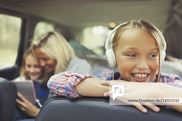 Lächelndes Mädchen hört Musik mit Kopfhörern auf dem Rücksitz des Autos.