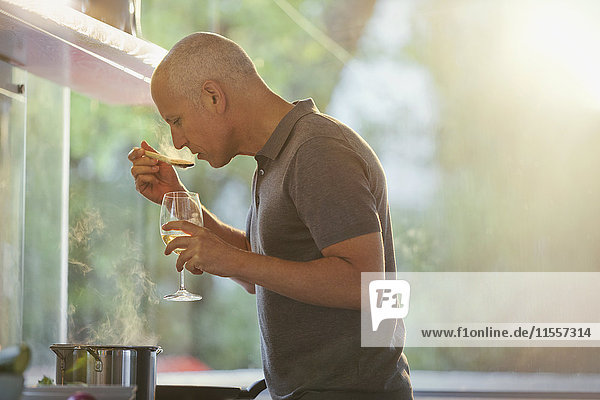 Man drinking white wine and cooking at stove in kitchen