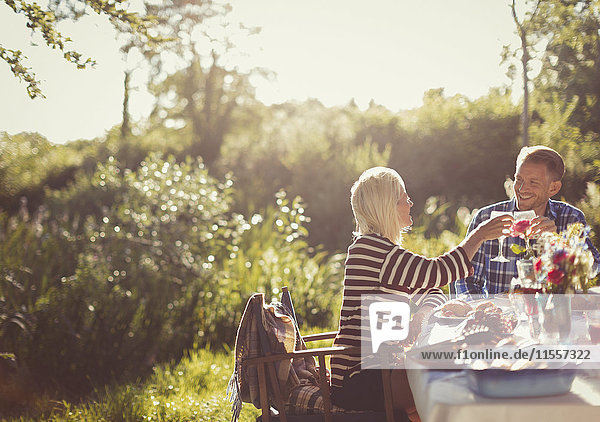Couple toasting wine glasses at sunny garden party patio table