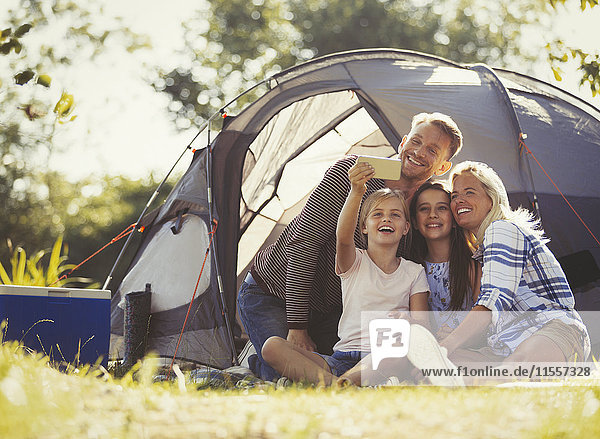 Familie nimmt Selfie mit Fotohandy vor dem Zelt auf dem sonnigen Campingplatz auf