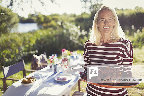 Portrait smiling woman serving platter of food at sunny garden party patio table